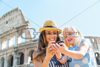 Happy mother and baby girl checking photos in camera near coloss