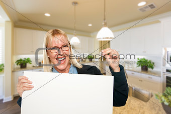 Young Woman Holding Blank Sign and Keys Inside Kitchen
