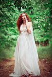 Beautiful redhead woman wearing white dress, in a forest