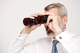 Male execuitve peers through binoculars