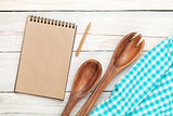 Notepad over kitchen towel and utensils on wooden table