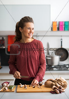Happy young housewife cutting mushrooms in kitchen