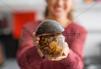 Closeup on happy young housewife showing jar of pickled mushroom