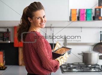 Happy young housewife holding baking dish with bread