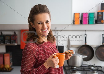 Portrait of happy young housewife drinking tea with freshly bake