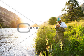Fly fisherman on the river bank at sunrise