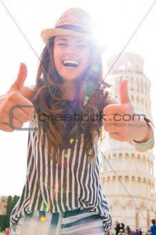 Happy young woman showing thumbs up in front of leaning tower of