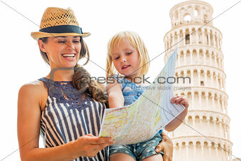 Happy mother and baby girl using map in front of leaning tower o