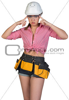 Woman in tool belt and hard hat adjusting protective glasses