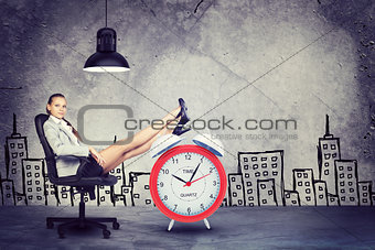 Businesswoman sitting with her feet up on alarm-clock 
