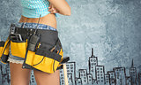 Woman in tool belt against stone wall with sketch of city on it