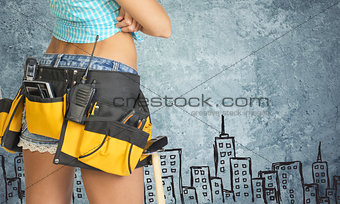 Woman in tool belt against stone wall with sketch of city on it