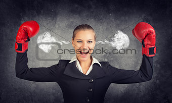 Businesswoman in boxing gloves posing with her arms up, shouting, smoke from ears