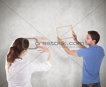 Composite image of couple deciding to hang picture