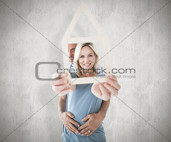 Composite image of happy couple holding house outline