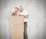Composite image of happy couple leaning on pile of moving boxes with piggy bank
