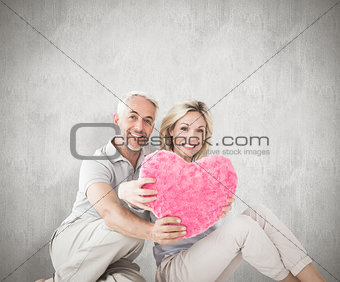Composite image of happy couple sitting and holding heart pillow