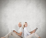 Composite image of happy couple sitting using laptop and tablet pc