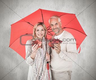 Composite image of smiling couple showing autumn leaves under umbrella