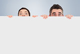 Composite image of man and woman hiding behind a white board with room for  copy space