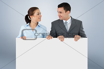 Composite image of business partners looking at each other while holding sign together
