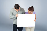 Composite image of young couple holding banner together and looking down
