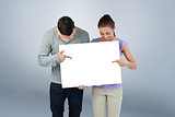 Composite image of young couple pointing at banner they are holding