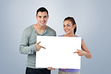 Composite image of smiling young couple pointing at sign they are holding