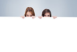 Composite image of two friends secretly hiding behind a blank poster