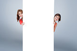 Composite image of teenage girls hiding behind a blank poster while showing their head from each sid