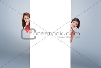 Composite image of teenage girls hiding behind a blank poster while showing their head from each sid