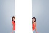 Composite image of two smiling teenage girls sitting behind a blank poster