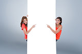 Composite image of teenage girls looking at the camera while pointing their fingers on a blank poste