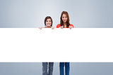 Composite image of smiling young women proudly holding a blank poster