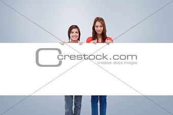 Composite image of smiling young women proudly holding a blank poster