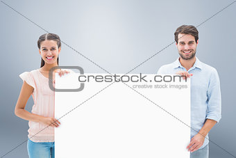 Composite image of attractive young couple smiling at camera holding poster