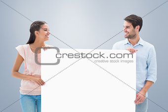 Composite image of attractive young couple smiling and holding poster