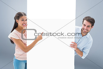 Composite image of attractive young couple smiling and holding poster
