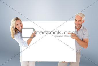 Composite image of happy couple holding and pointing to large poster