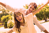Attractive couple smiling at camera and spreading arms in the park