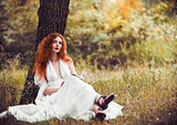 Lovely redhead woman sitting under tree and reading a book