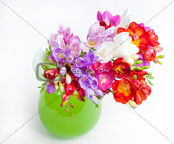 Beautiful bouquet of colorful freesia in green vase on a white b