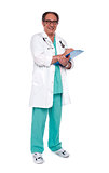 Aged doctor holding clipboard. Full length shot