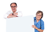 Two matured doctors holding white banner ad