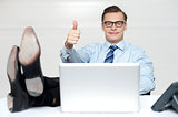 Thumbs up guy relaxing with legs on work desk
