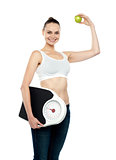 Fit woman holding weighing machine and green apple
