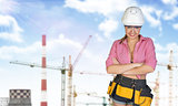 Woman in tool belt and helmet. Tower cranes, chimneys as backdrop