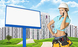 Woman in tool belt using phone. Green hills, road, buildings and billboard as backdrop