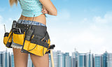 Woman in tool belt stands back. Building and sky as backdrop