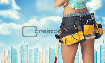 Woman in tool belt stands back, crossed arms. Cropped image. Wire-frame buildings as backdrop